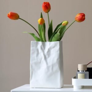 Pleated square matte white ceramic flower container, distinct wrinkled bag silhouette, wide opening bloom holder for table focal displays in residential and work spaces